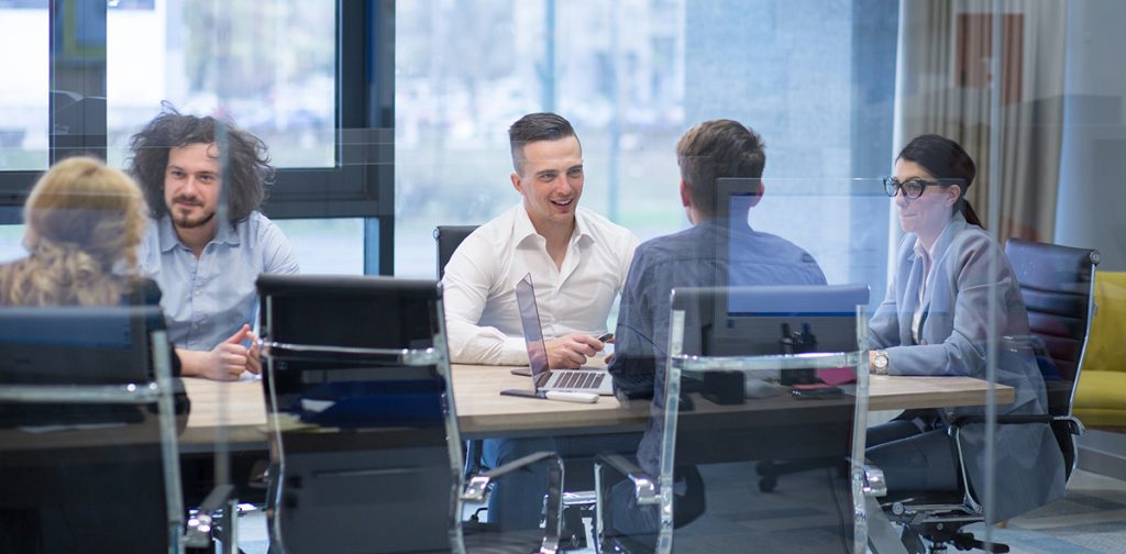 group of people with exisiting relationship stilling around an office table and talking about custom application development